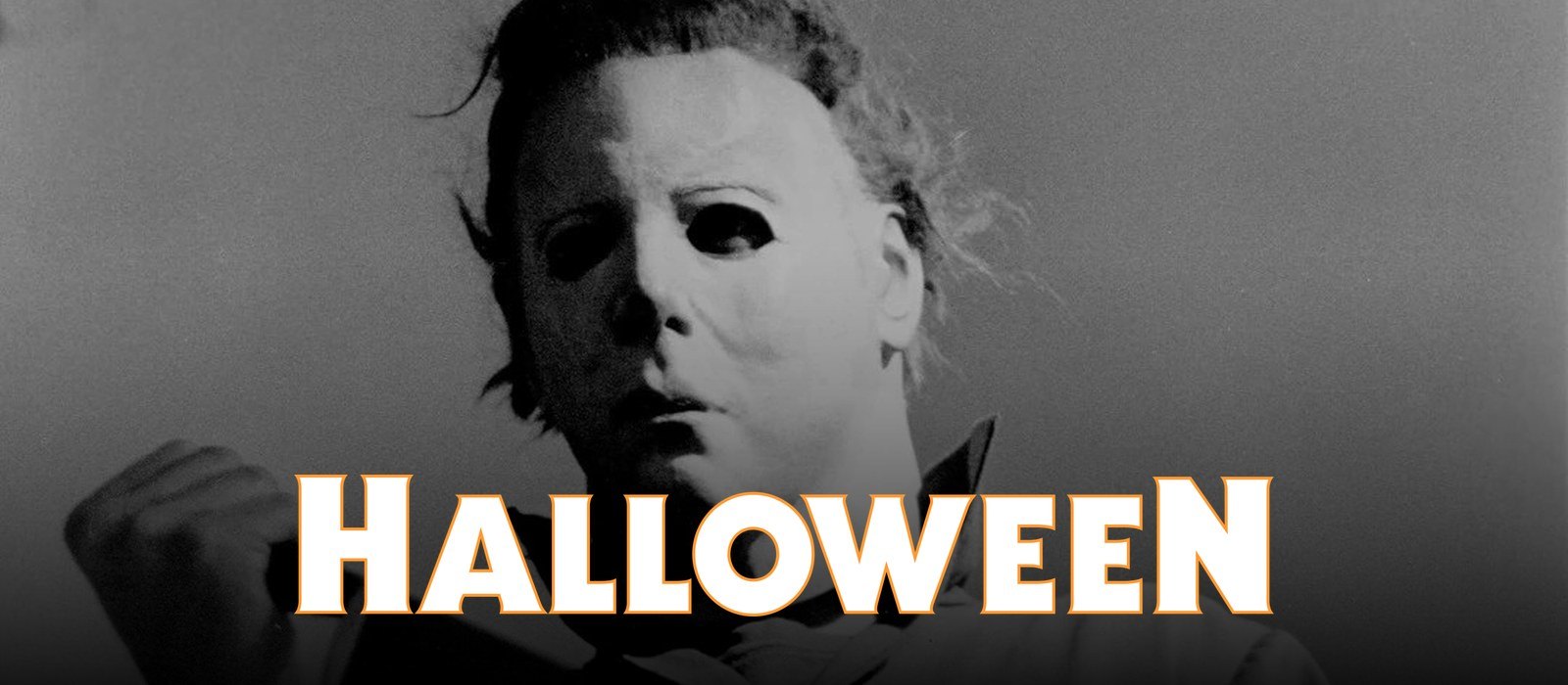 Close-up of Michael Myers in his white mask, from a 1978 publicity photo, with the orange-outlined HALLOWEEN title logo across the bottom.