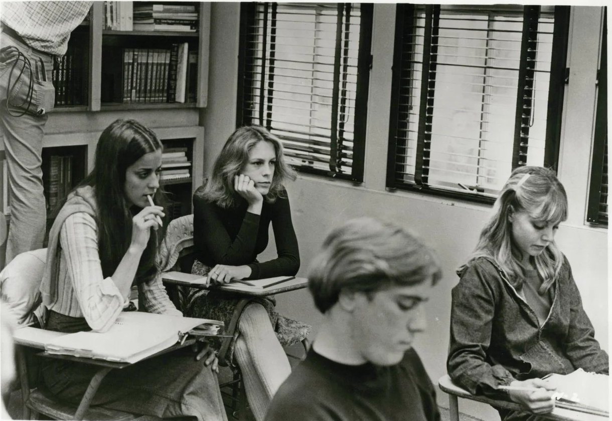Four students at classroom desks in a black-and-white publicity photo; Jamie Lee Curtis, second from left, rests her chin on her hand.