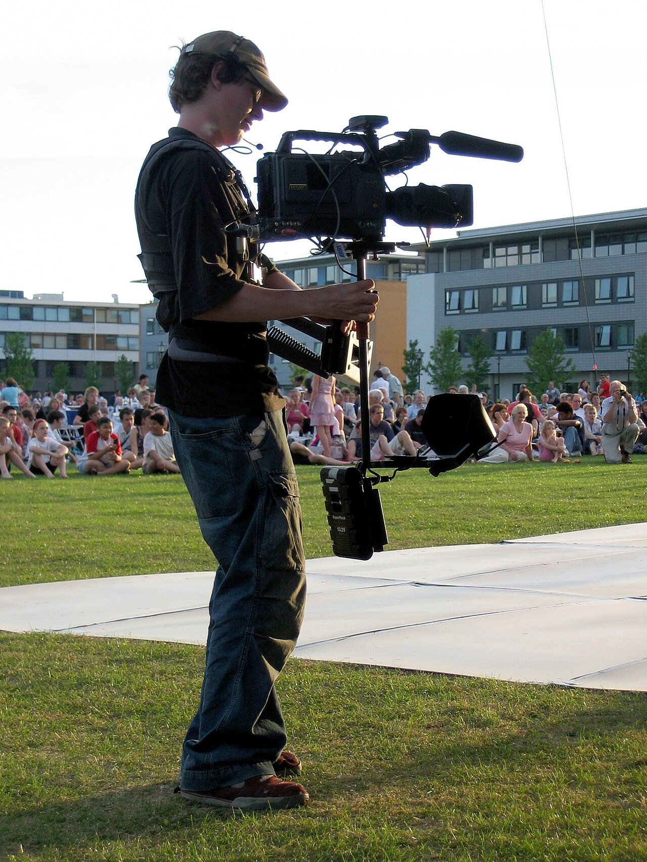 A camera operator wearing a Steadicam rig, with the camera on an arm from a vest, filming in front of a crowd.