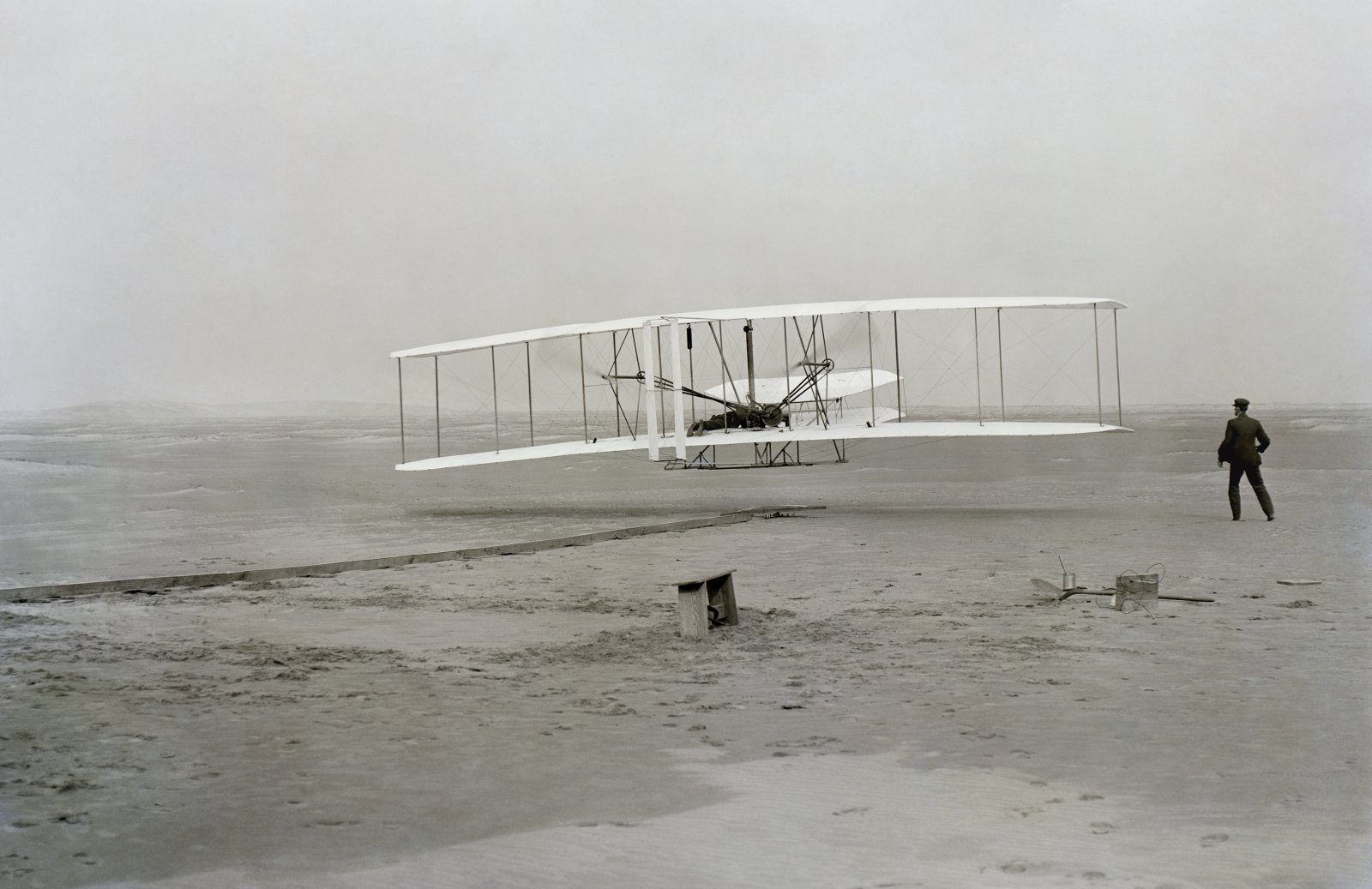The Wright Flyer lifting off the sand at Kitty Hawk on December 17, 1903, with Wilbur Wright standing to the right